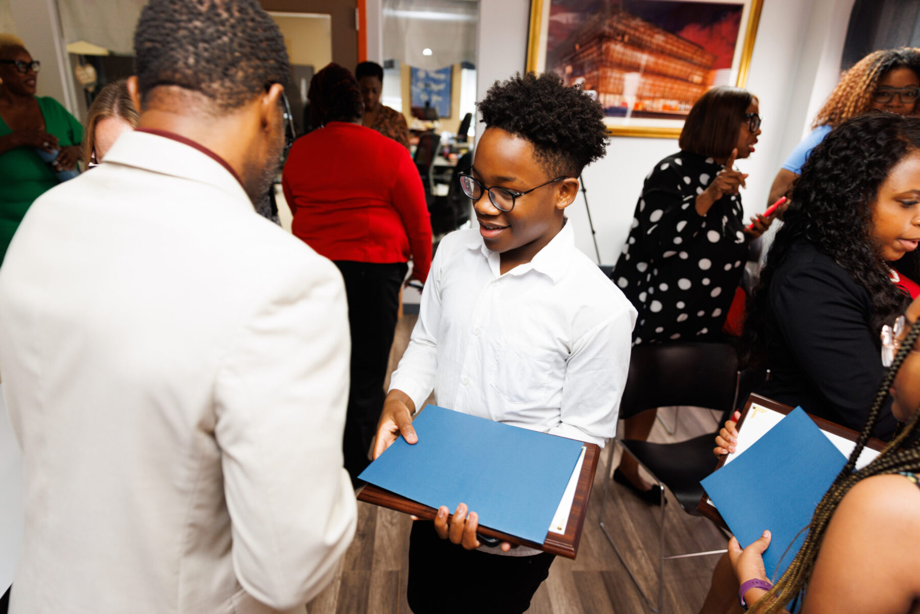 A Y-KNOT student presenting a certificate at an awards ceremony, surrounded by staff and supporters